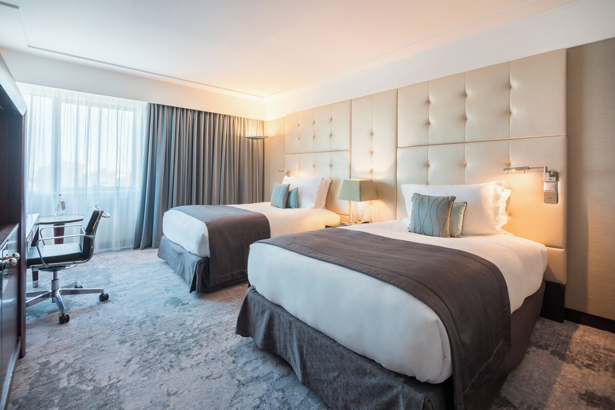 A hotel room with two beds, a desk, and a chair.