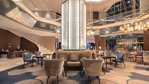 Een moderne hotel lobby met een centrale kolom, zithoek en een trap.