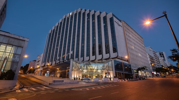 Een modern hotel met een glazen gevel, een opvallende entree en een parkeerplaats.
