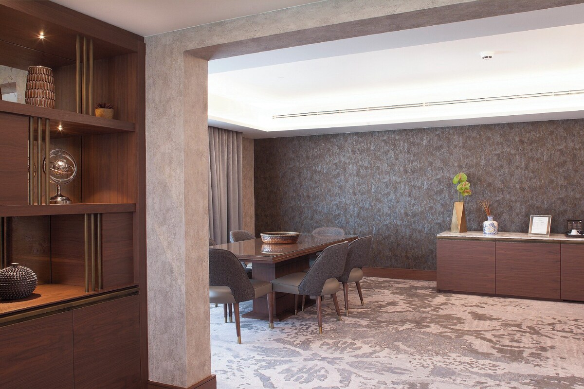 A modern hotel room with a dining area, a wooden bookshelf, and a reception desk.