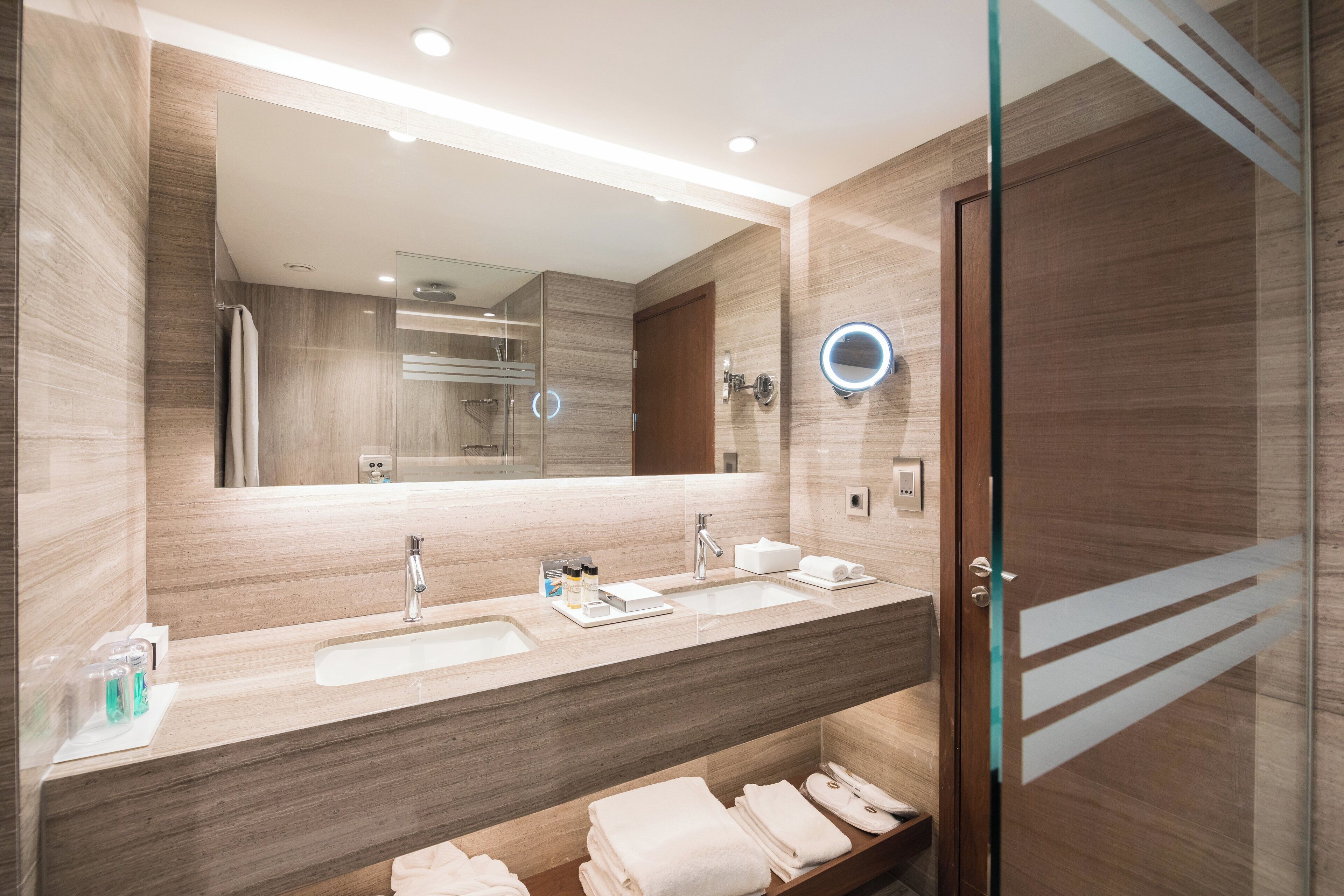 Un baño moderno con un espejo grande, dos lavamanos y una cabina de ducha de vidrio.