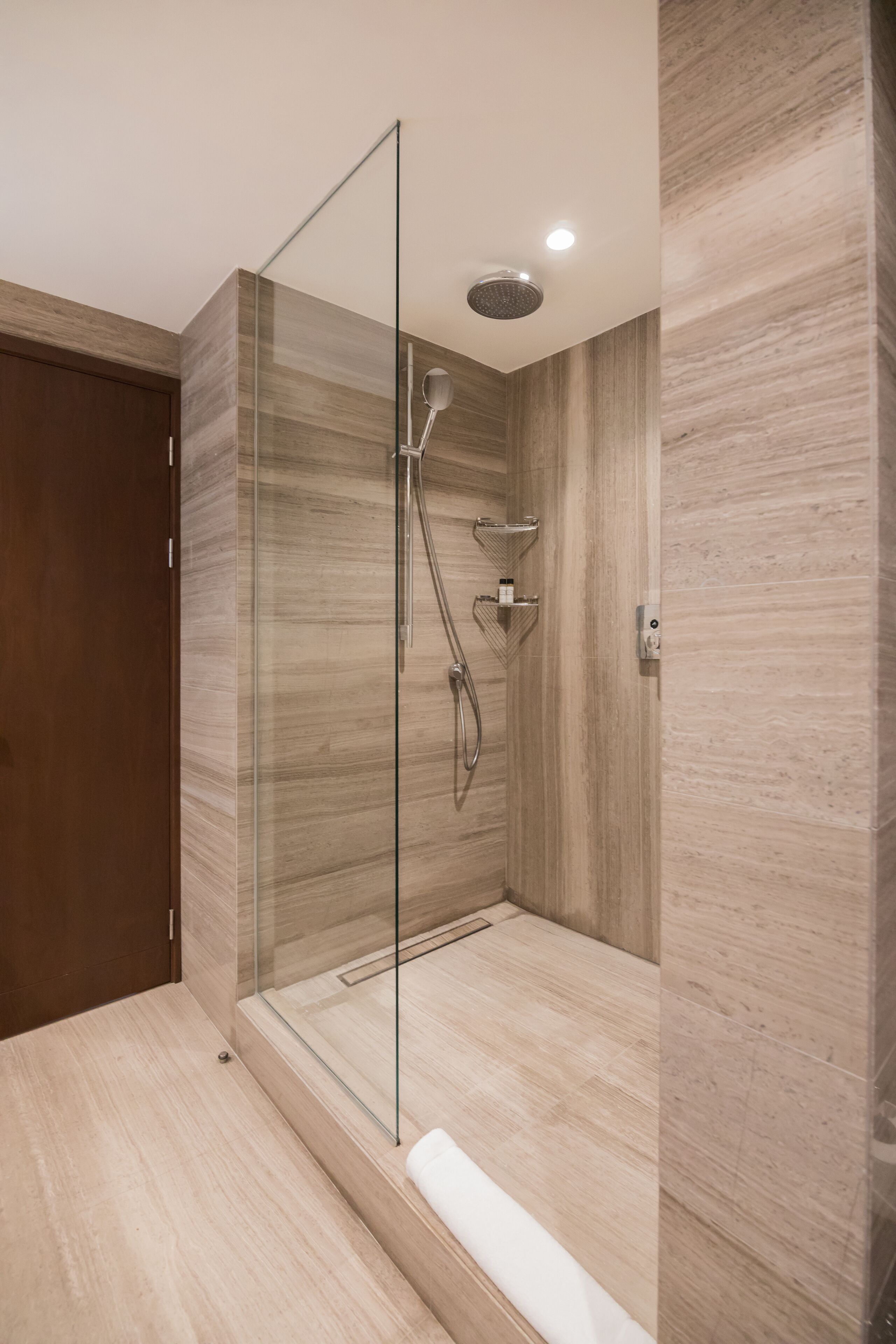 A modern shower with a glass door, wooden walls, and a built-in shelf.