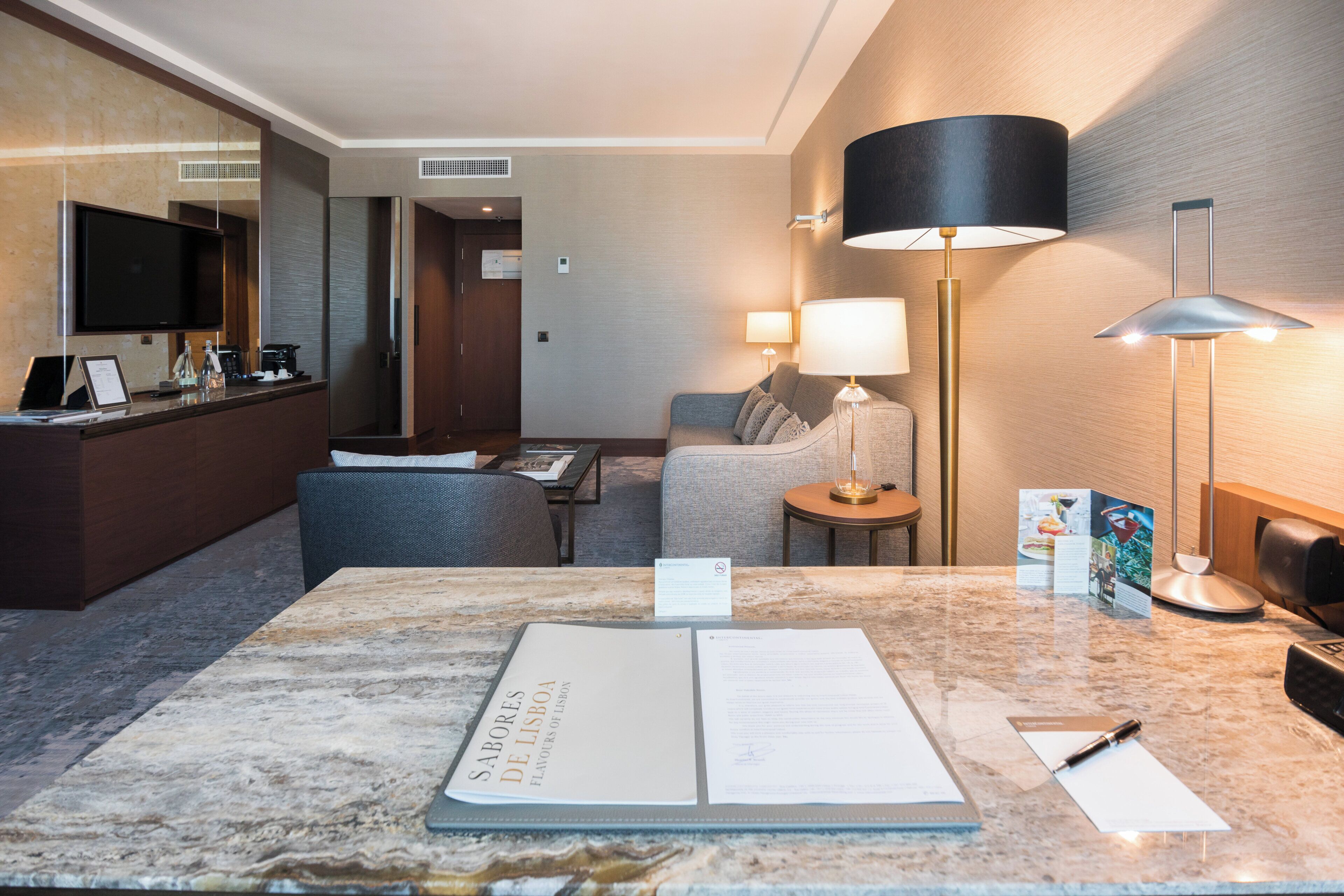 A hotel room with a marble reception desk, a sofa, a small table, and a lamp.