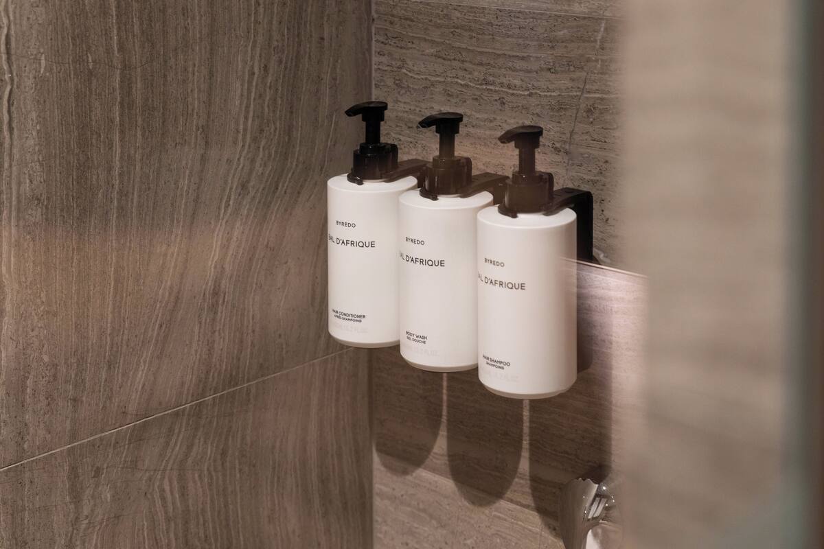 Three white bottles with black pumps labeled 'SYREDO' on a tiled wall.