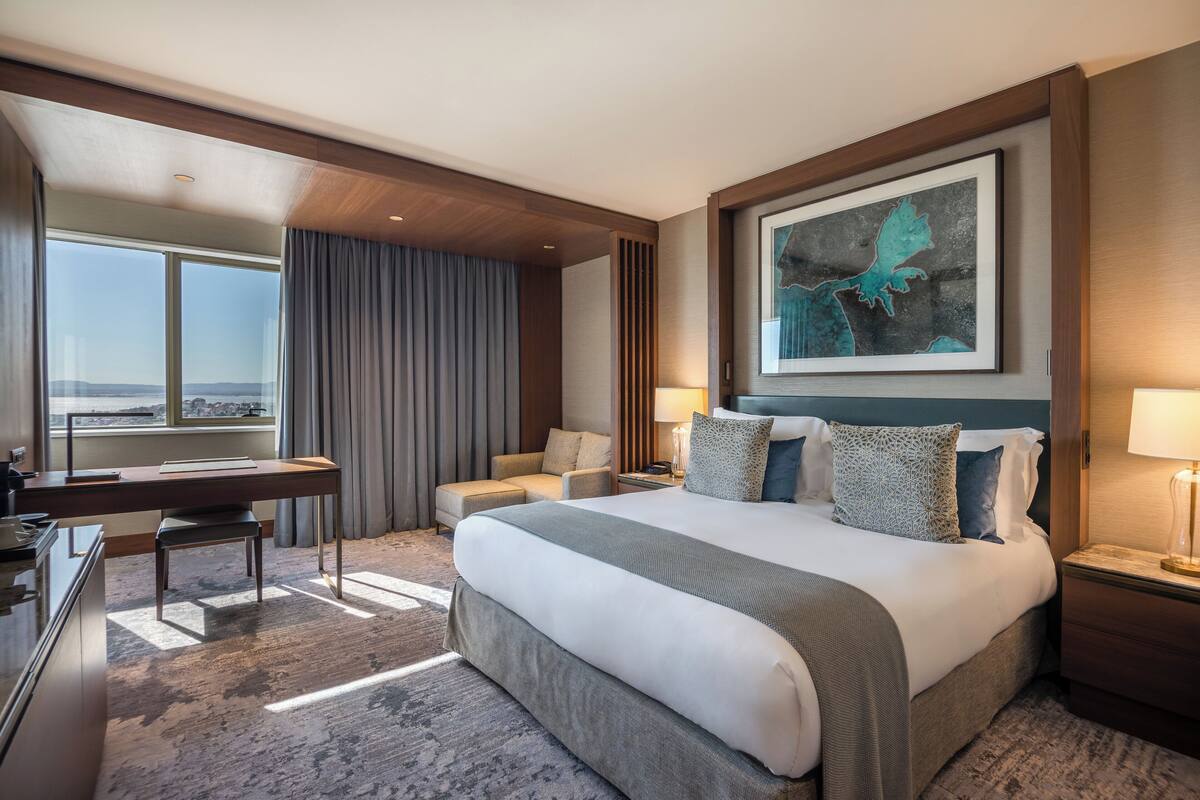 A modern hotel room with a large bed, a desk, and a view of the city.