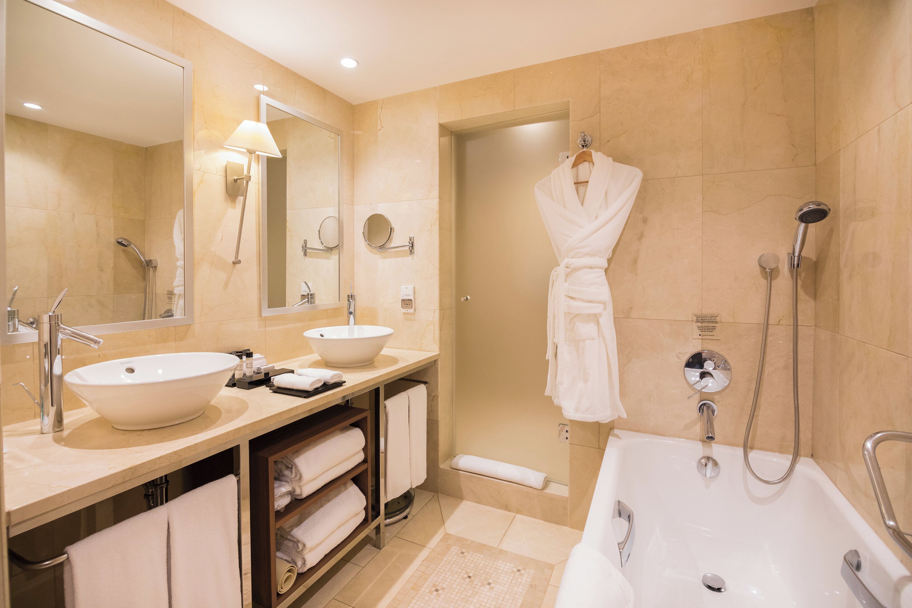 A modern bathroom with two sinks, a large mirror, a walk-in shower, and a bathtub.