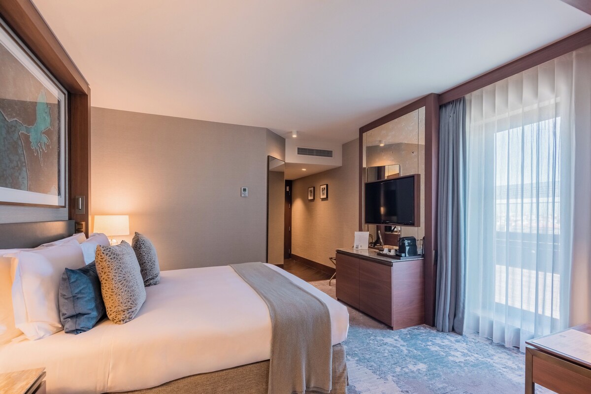 Habitación de hotel con una cama grande, un escritorio, un televisor y vistas al exterior.