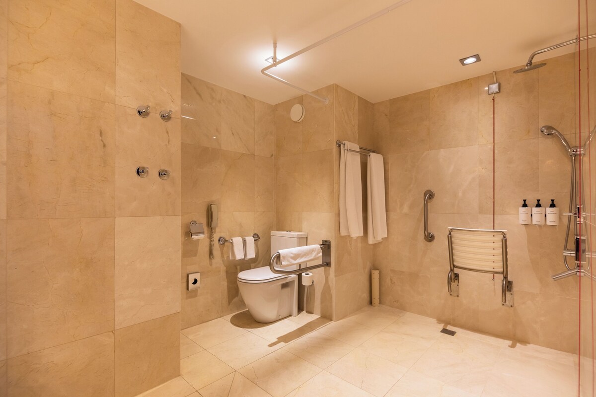A modern bathroom with a toilet, shower, and handrails.