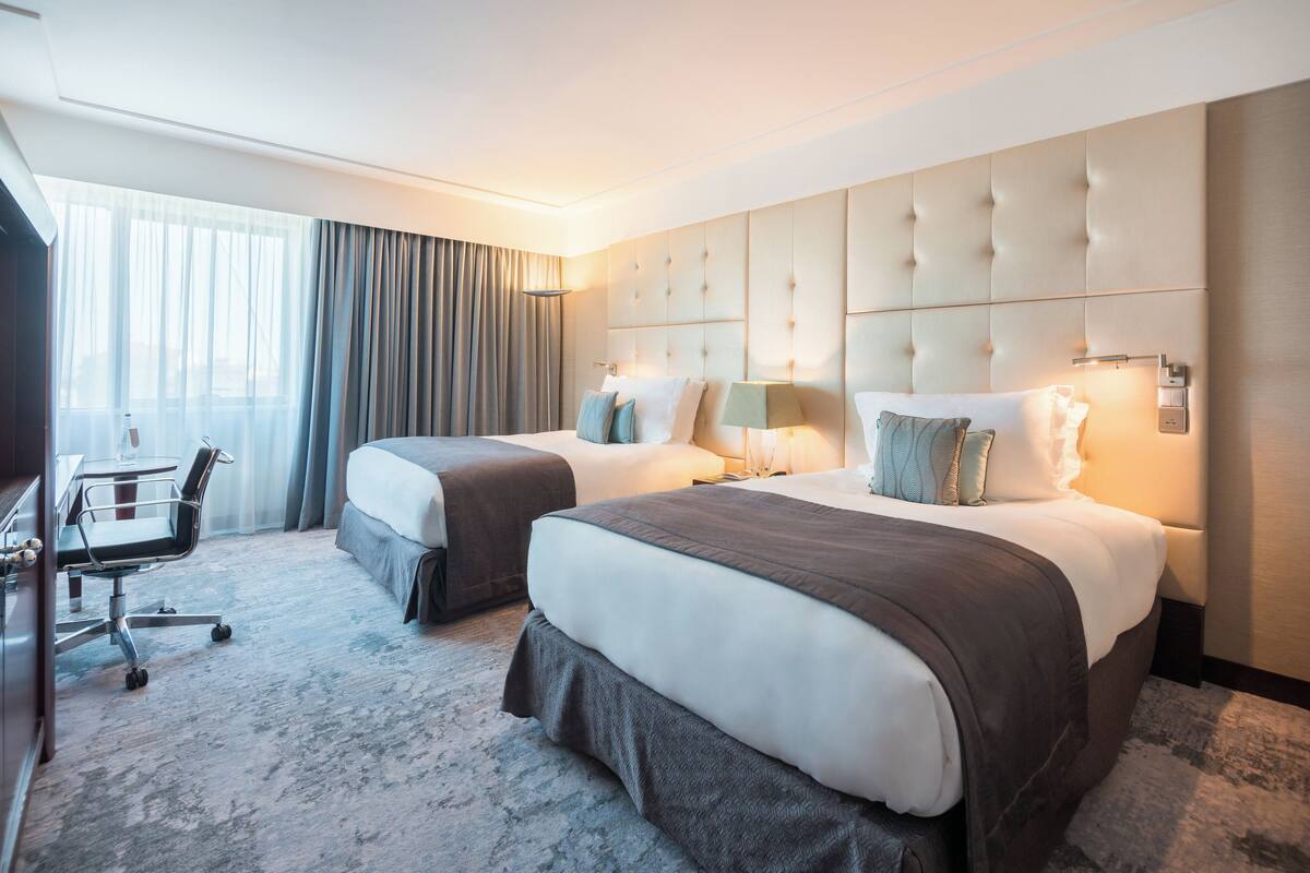 A hotel room with two beds, a desk, and a chair.