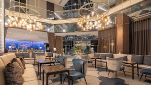 Een ruime lobby met een moderne kroonluchter, comfortabele zithoeken en een groot scherm.'