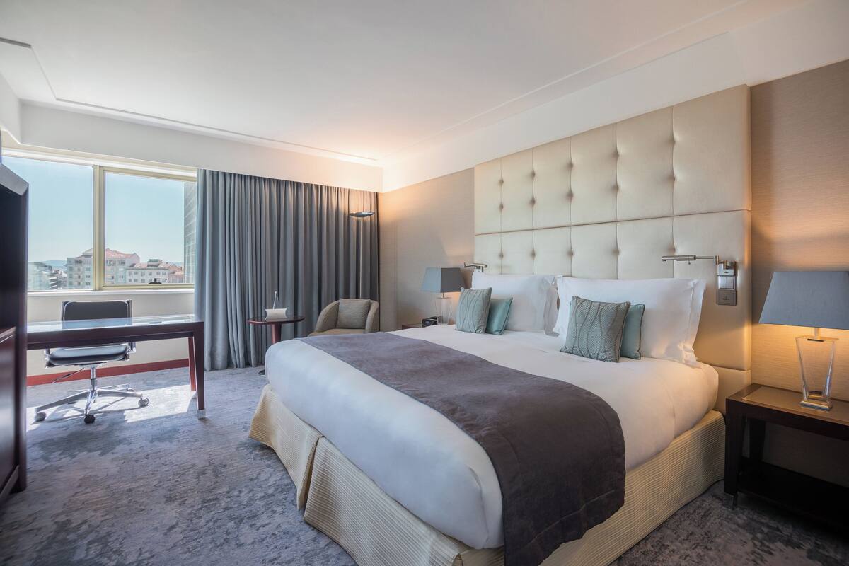 A hotel room with a large bed, a desk, and a chair.
