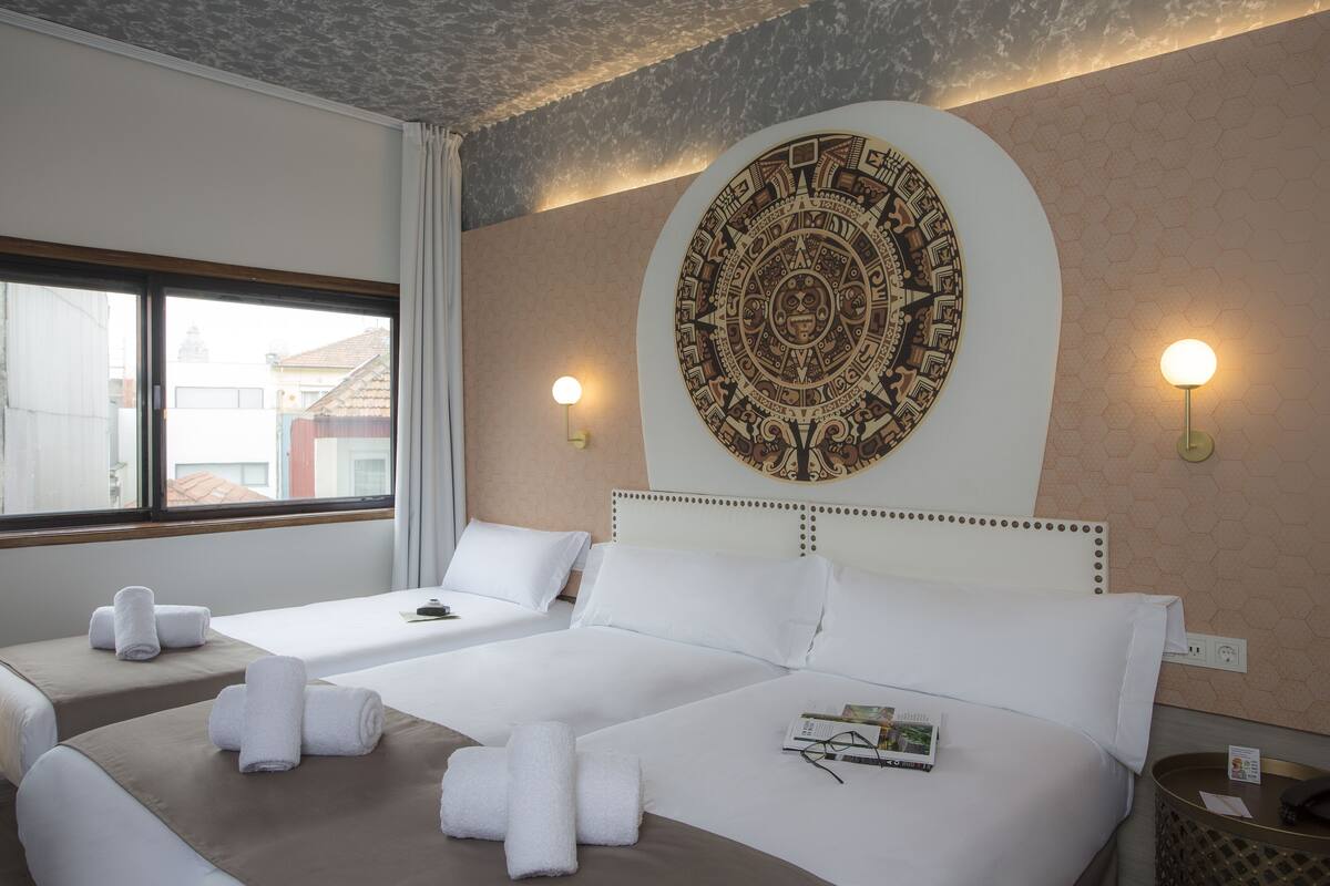 A hotel room with two beds, a large decorative wall piece, and two wall-mounted lamps.