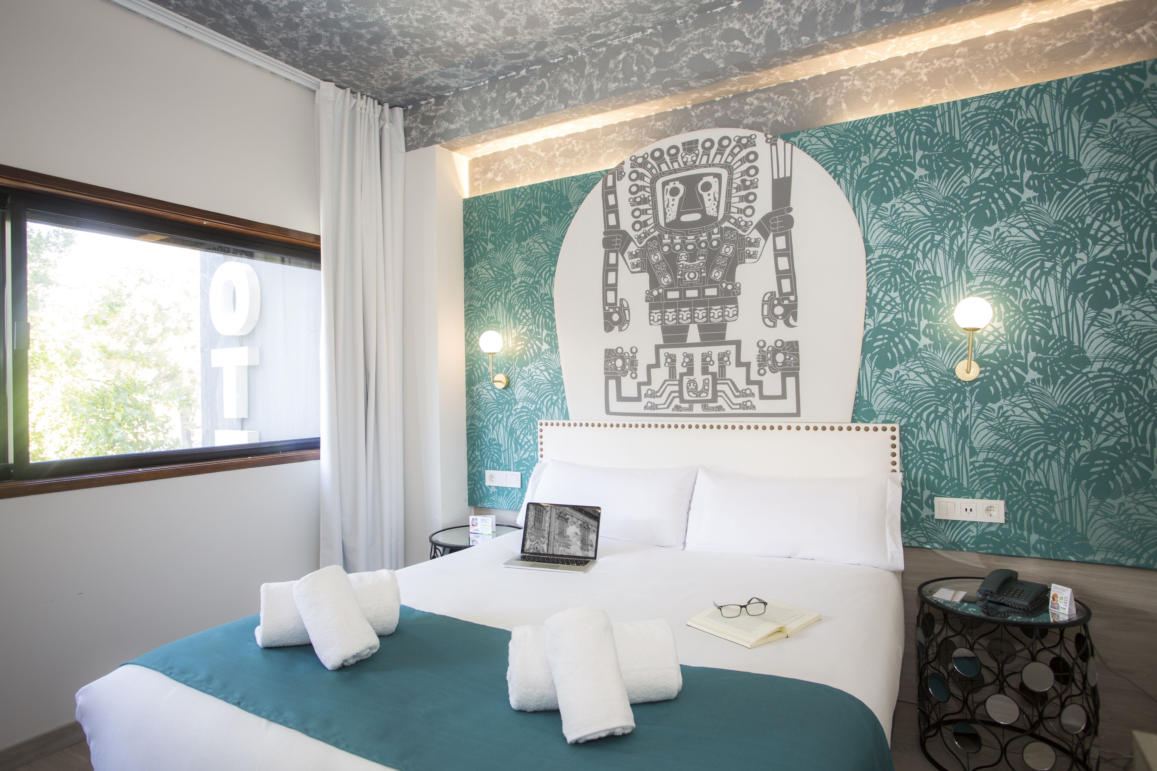 Een hotelkamer met een bed, een laptop, een boek en een telefoon op een nachtkastje.