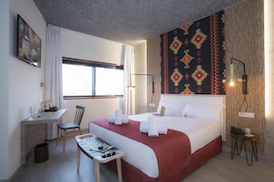 A hotel room with a bed, desk, chair, and a small table with a magazine.