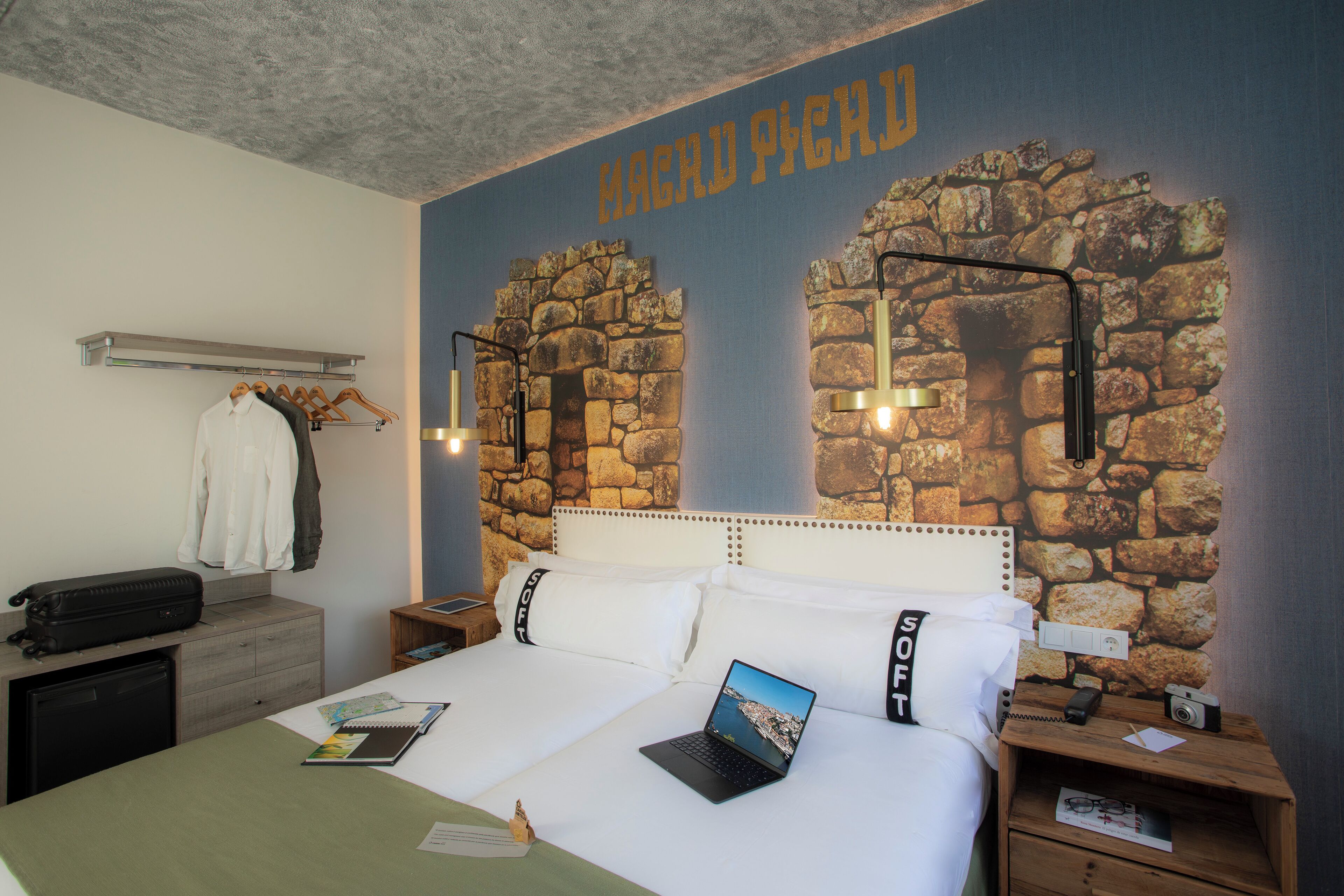 Camera d'hotel con un letto, una scrivania, un armadio e una parete in pietra con la scritta "MAGADY PICHIO".