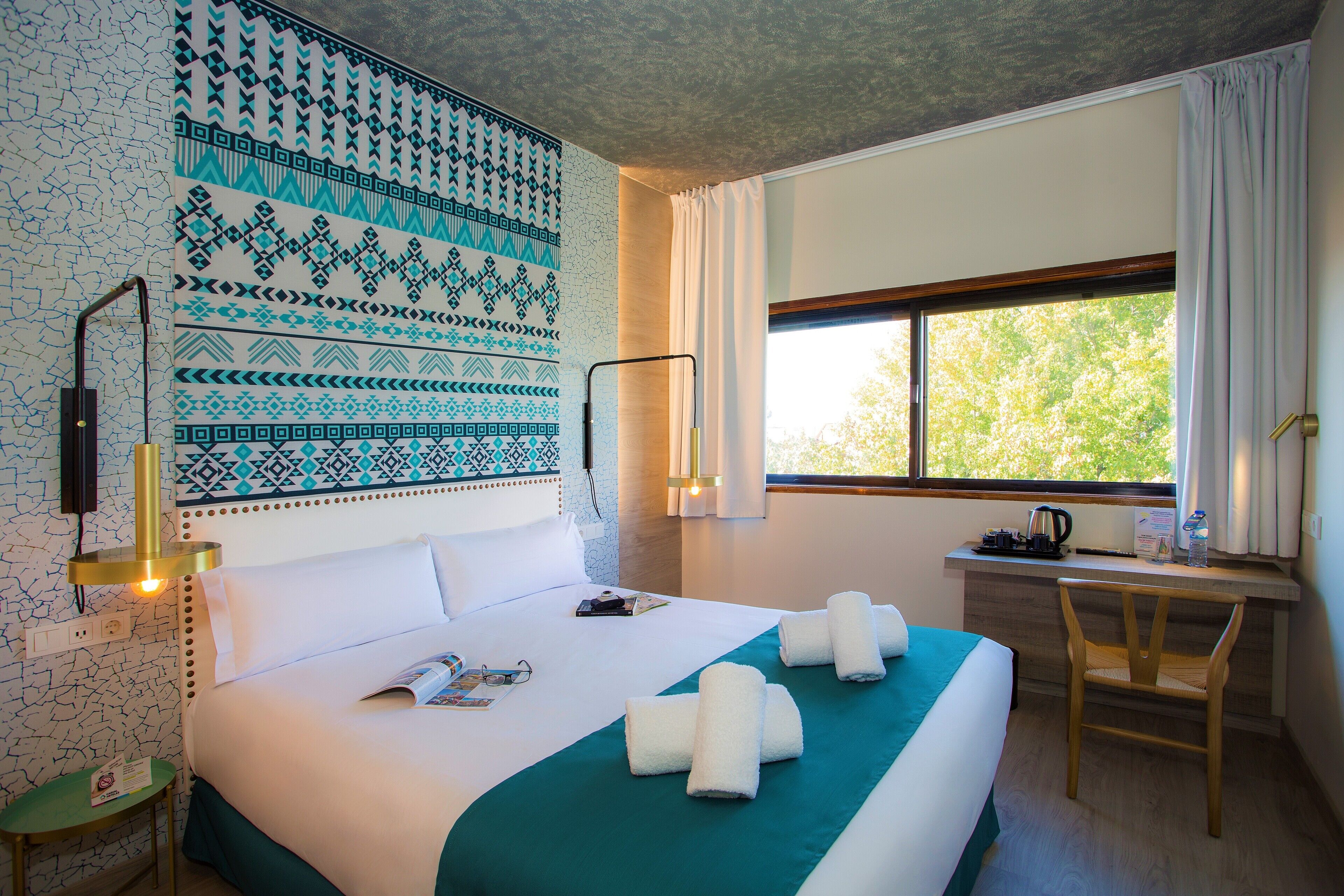A hotel room with a large bed, a desk, and a window with a view of trees.