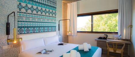 A hotel room with a large bed, a desk, and a window with a view of trees.