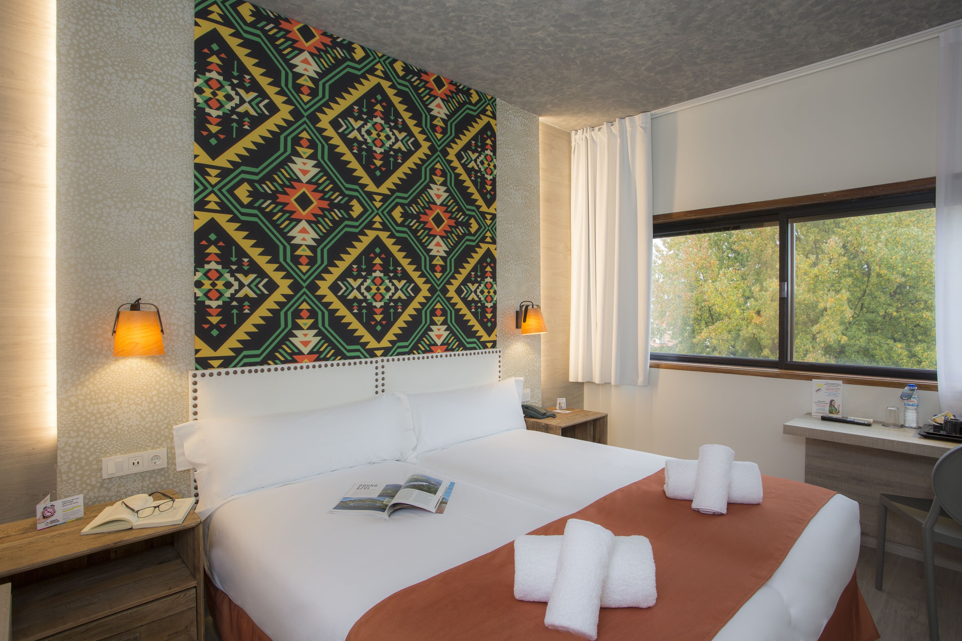 Habitación de hotel con cama, escritorio, ventana y un tapiz decorativo en la pared.