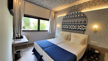 Hotellihuone, jossa on suuri sänky, työpöytä tuolilla, ikkuna verhoilla ja kuvioitu seinä.
