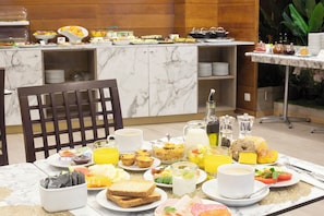 Een ontbijtbuffet met diverse gerechten en drankjes, een marmeren aanrecht en een houten stoel.
