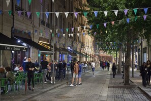 A street lined with outdoor seating at various cafes, with people dining and walking.
