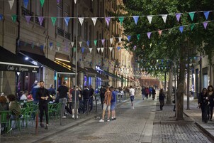 A street lined with outdoor seating at various cafes, with people dining and walking.