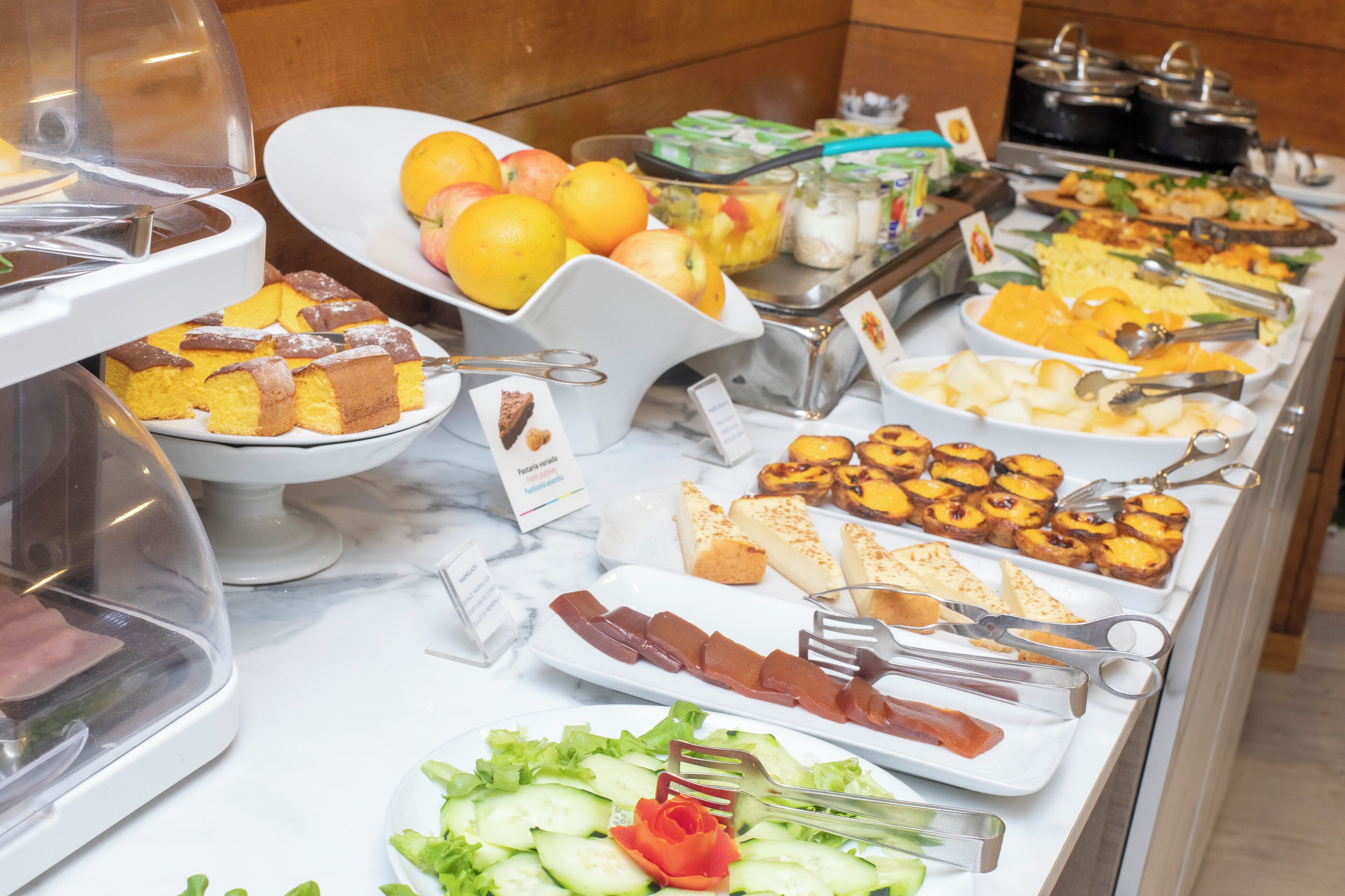 Un bufé con diversas opciones de comida, entre ellas frutas, pasteles y ensaladas.
