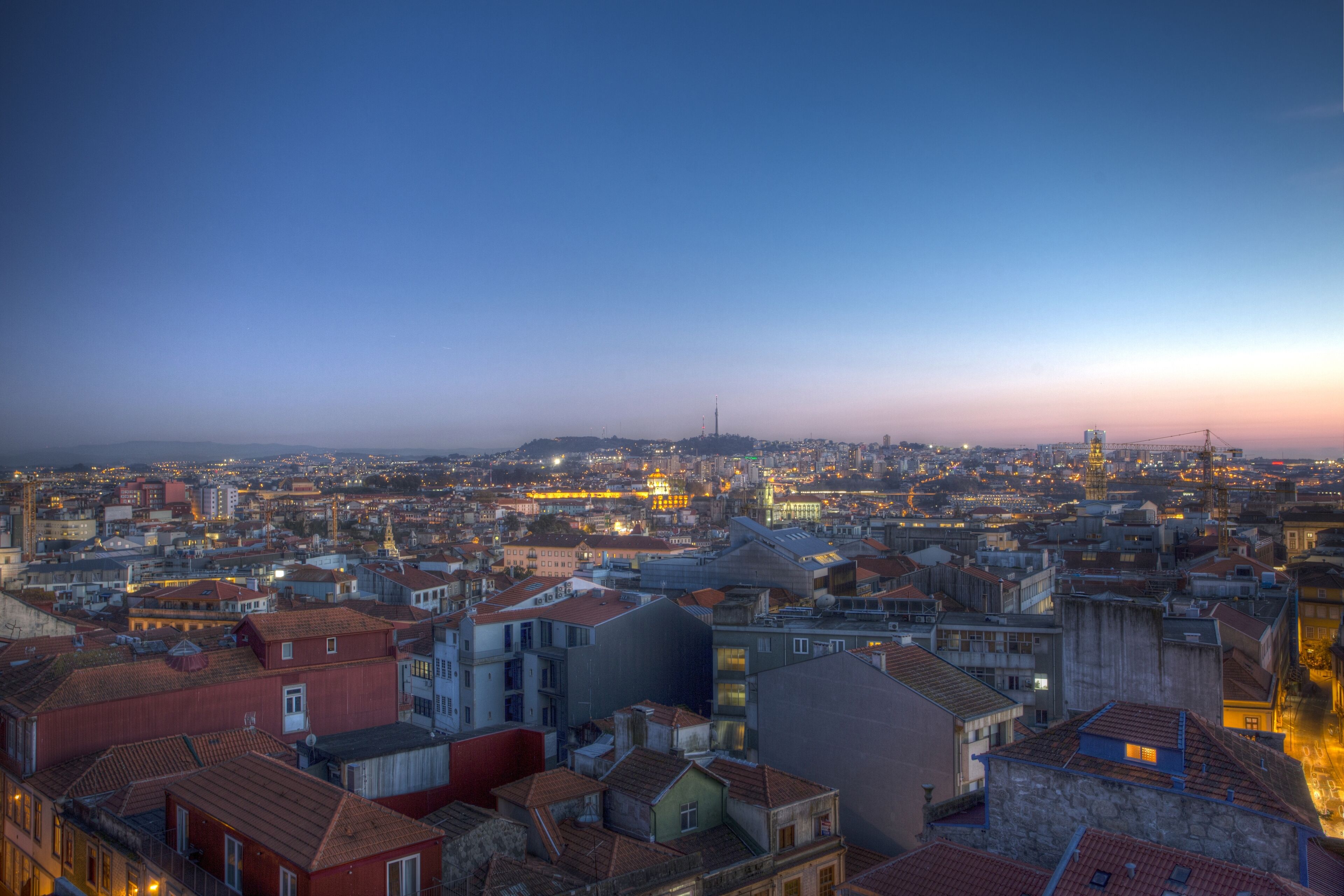 A cityscape at dusk with a variety of building styles and a prominent tower in the distance.