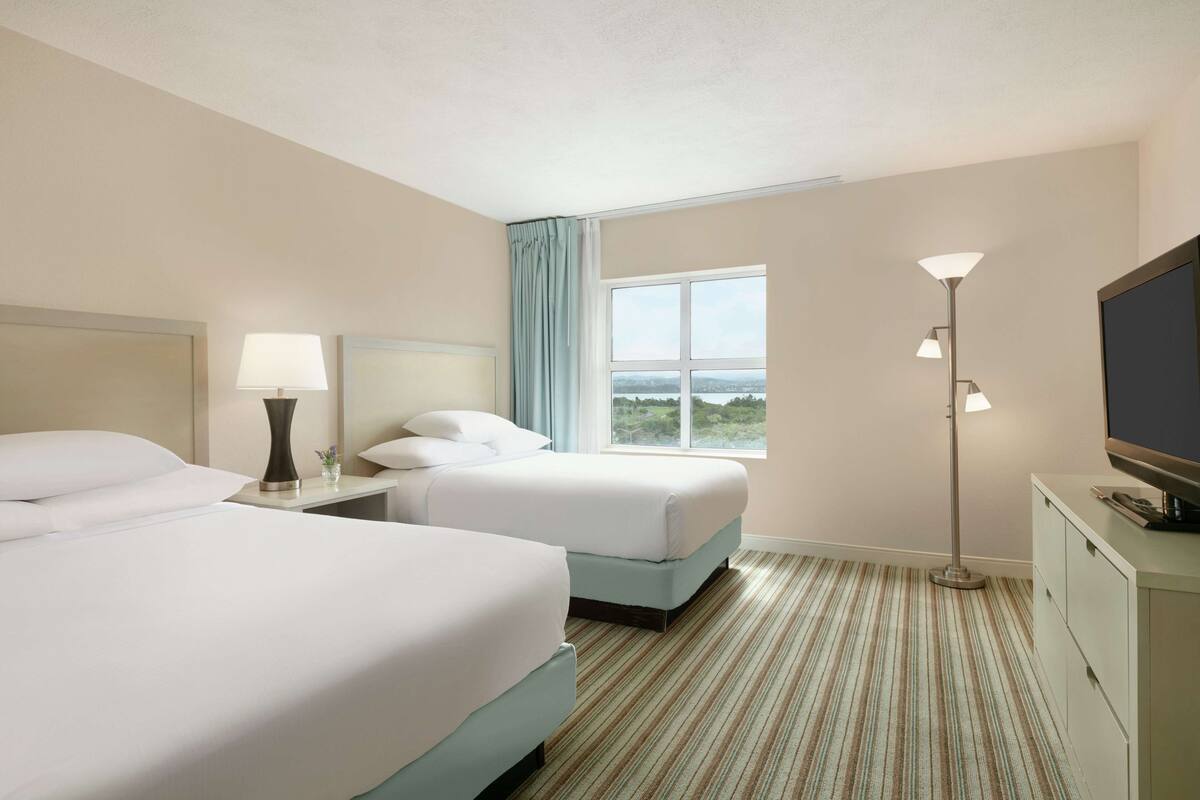 Quarto de hotel com duas camas, televisão, escrivaninha e janela com vista.