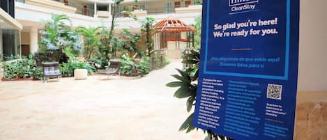 A Hilton CleanStay sign in a hotel atrium with a view of the building's interior and outdoor seating area.