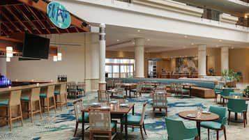 A spacious hotel lobby with multiple seating areas, a bar, and a large staircase.
