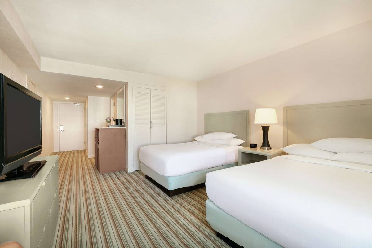 Quarto de hotel com duas camas, uma televisão, uma escrivaninha e um espelho.