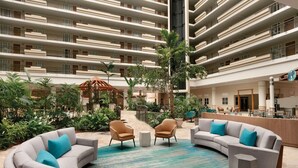 A hotel lobby with a curved grey sofa set, a small round table, and a reception desk. - Embassy Suites by Hilton San Juan Hotel & Casino (Carolina)
