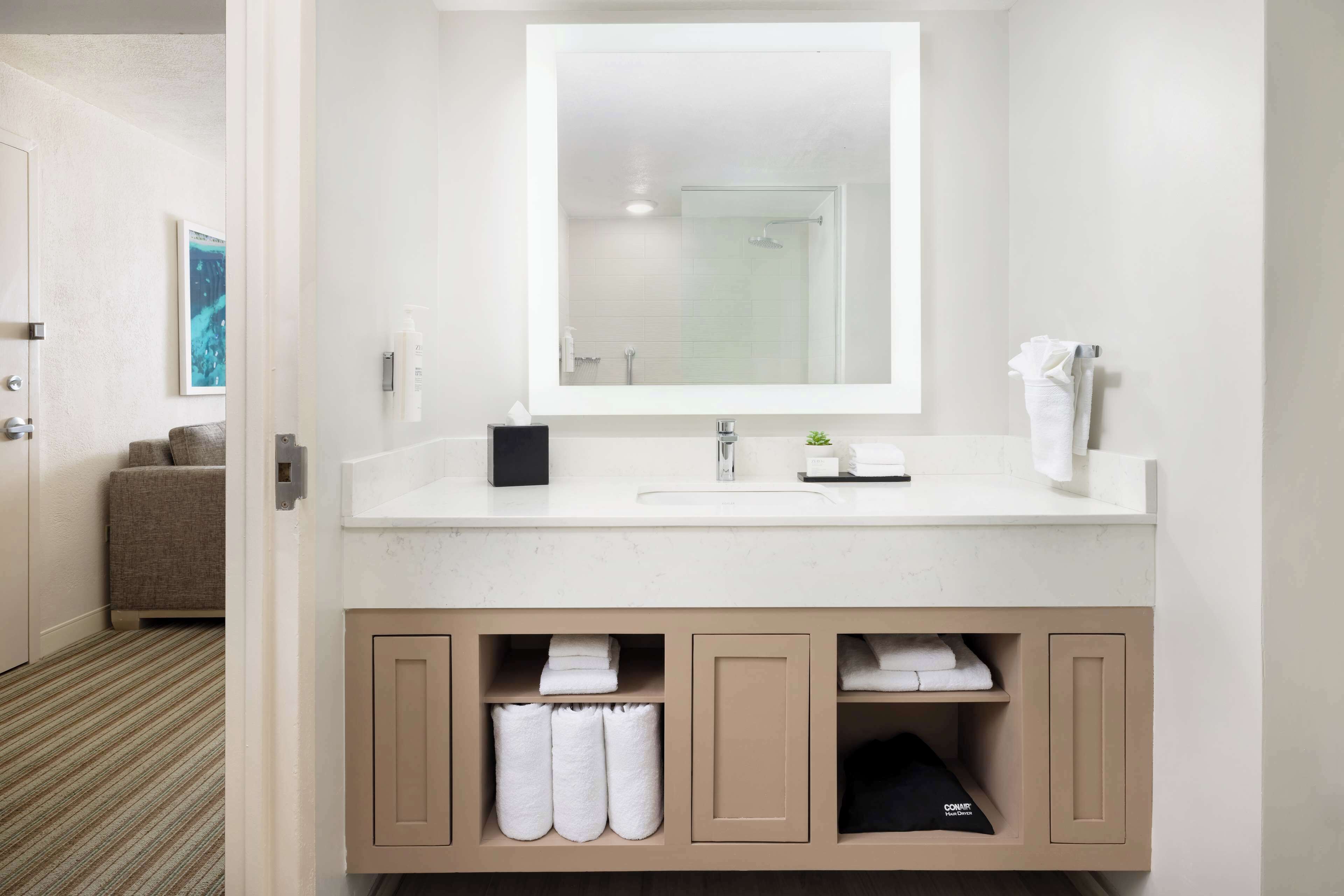 A modern bathroom with a large mirror, white sink, and storage cabinets.