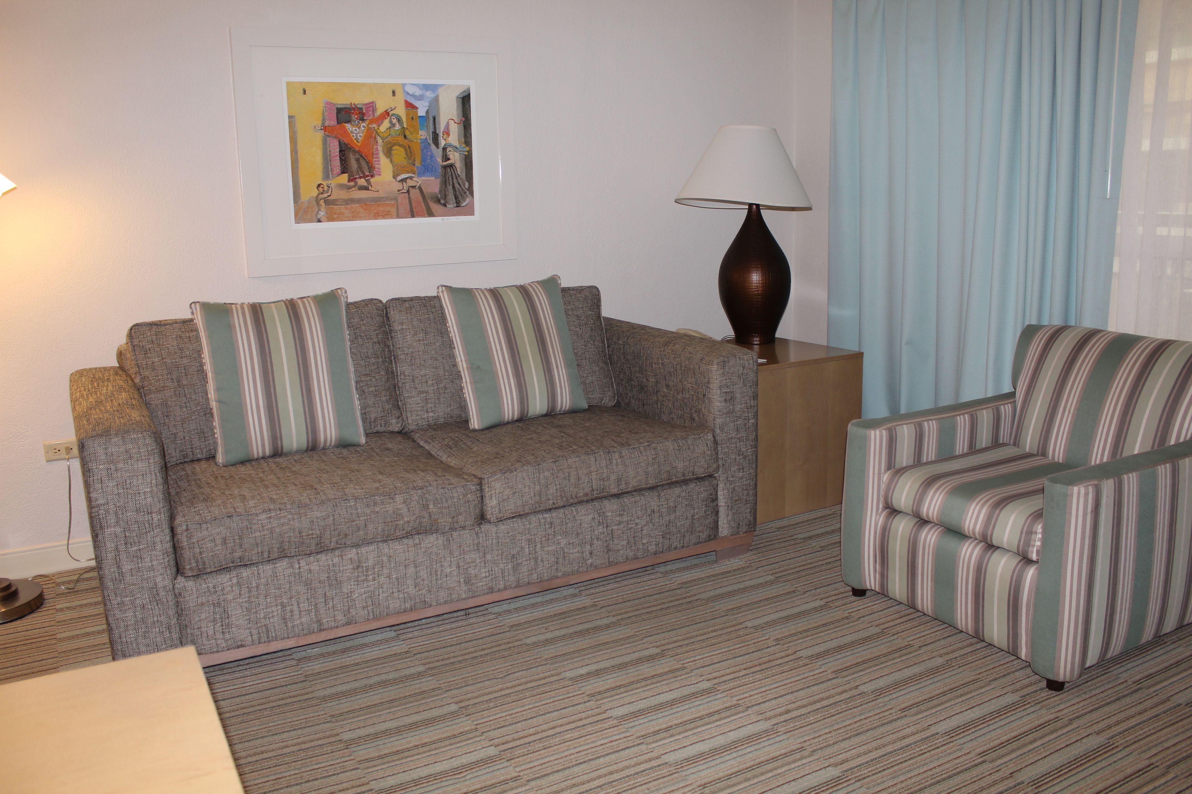 A living room with a grey sofa, striped armchair, and a lamp.