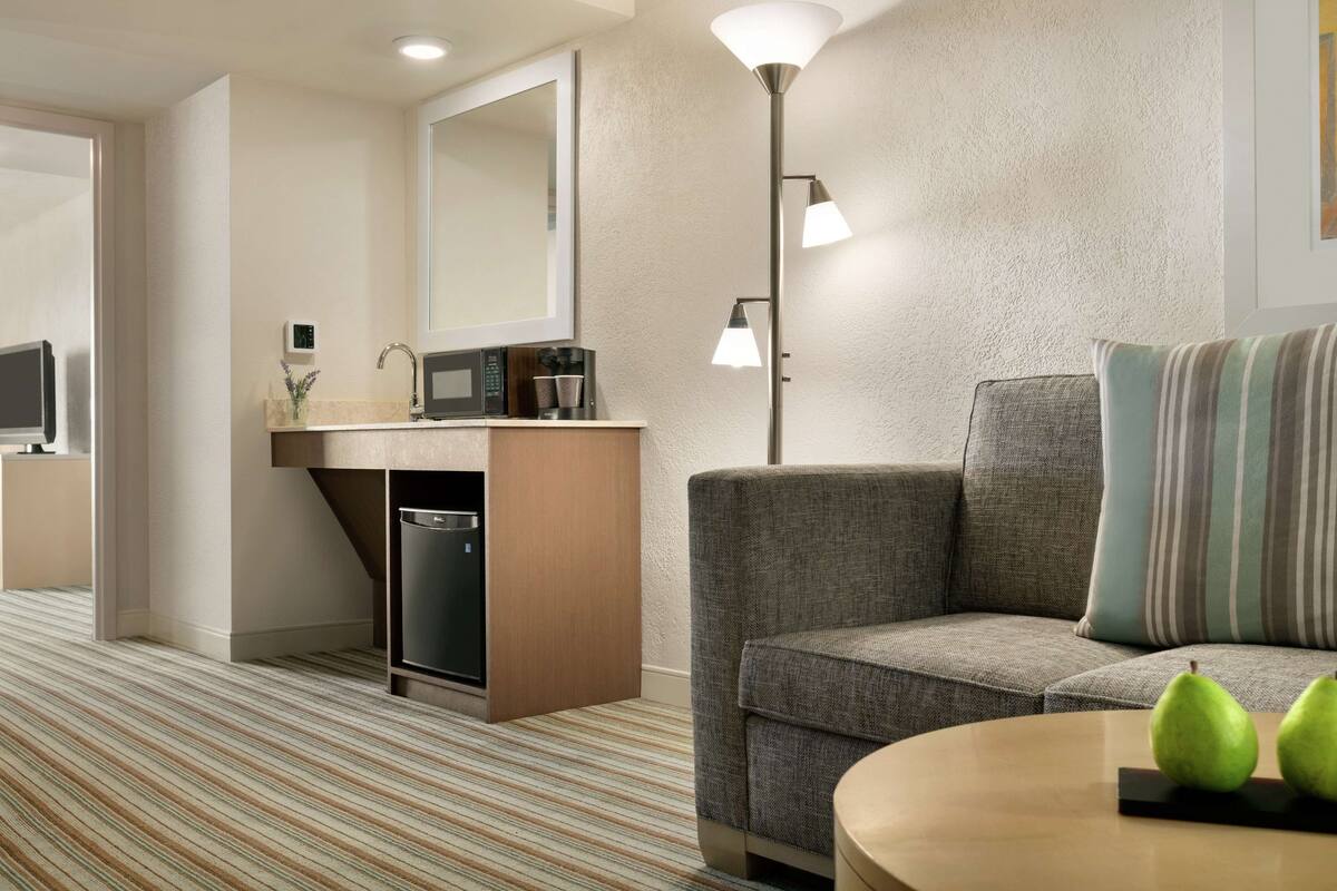 Quarto de hotel moderno com sofá, uma mesinha, micro-ondas, cafeteira e abajur.