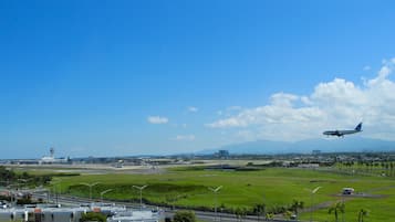 Pista de aeroporto com um avião decolando, cercada por campos verdes e céu claro.