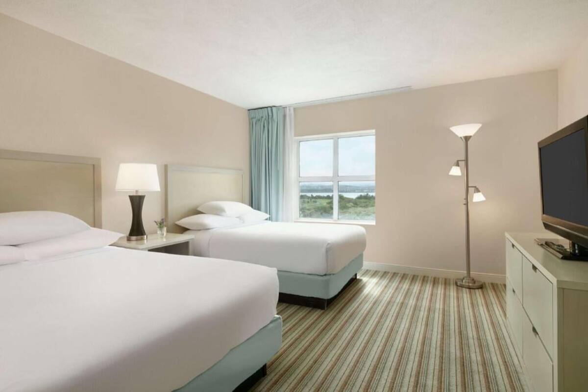 Quarto de hotel com duas camas, uma janela ampla com vista, televisão e abajur.