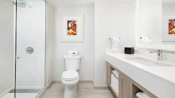 Un baño moderno con cabina de ducha de vidrio, inodoro blanco, lavamanos con espejo y una obra de arte enmarcada en la pared.