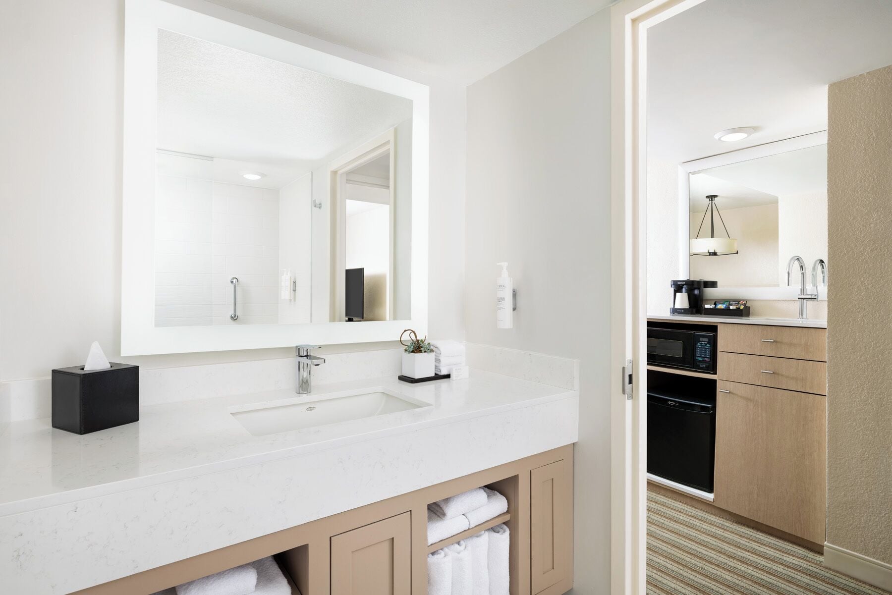 Une salle de bain moderne avec un grand miroir, deux lavabos et une machine à café.
