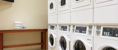 A laundry area with multiple stacked washing machines and a table with folded towels and a bottle.