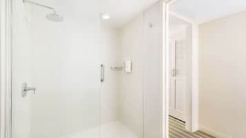 A modern bathroom with a glass shower enclosure, white tiled walls, and a visible toilet paper dispenser.