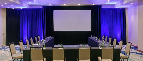 A conference room with a large table, chairs, a screen, and curtains.