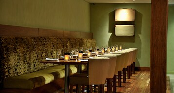 Une longue table à manger, décorée de bougies, entourée de chaises et agrémentée d’un banc à motifs, dans un restaurant.