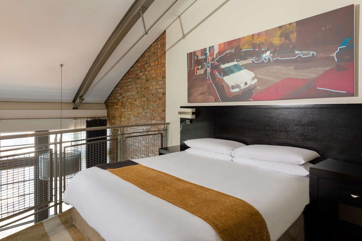 A modern hotel room with a large bed, a headboard, a nightstand, and a large abstract painting on the wall.