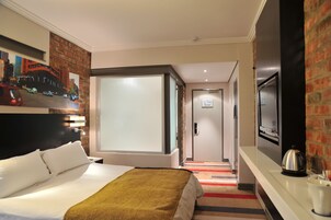 A hotel room with a bed, a television, a painting, and a door leading to another room.