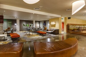 A modern hotel lobby with leather seating, a reception desk, and a television.