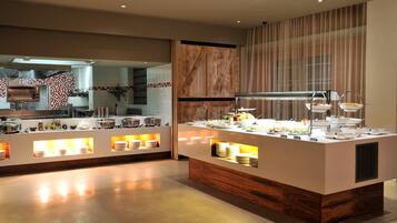 A modern buffet setup with multiple serving stations, a kitchen area in the background, and a wooden accent wall.