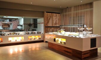 A modern buffet setup with multiple serving stations, a kitchen area in the background, and a wooden accent wall.