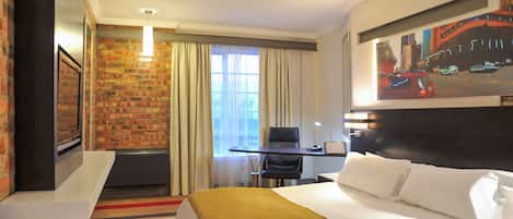 Habitación de hotel con cama, escritorio, silla, ventana con cortinas y un cuadro en la pared.